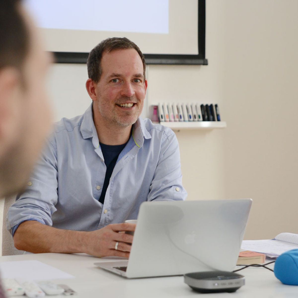 Sven Krieger lächelnd am Laptop im Seminarraum, vorn unscharf ein Teilnehmer