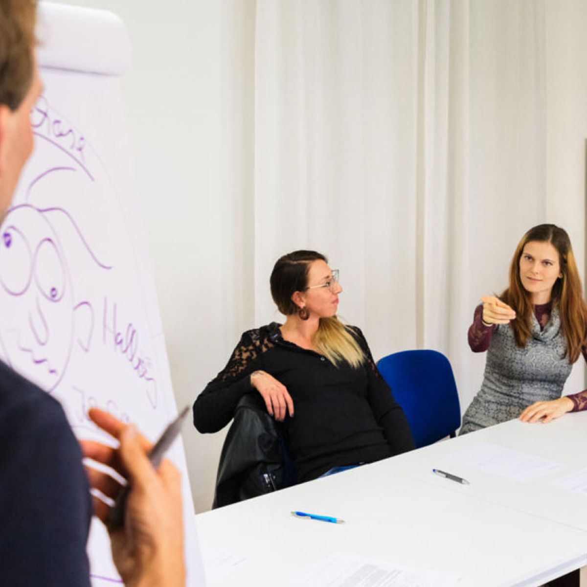 Dozent am Flipchart vor drei Teilnehmerinnen im Seminarraum