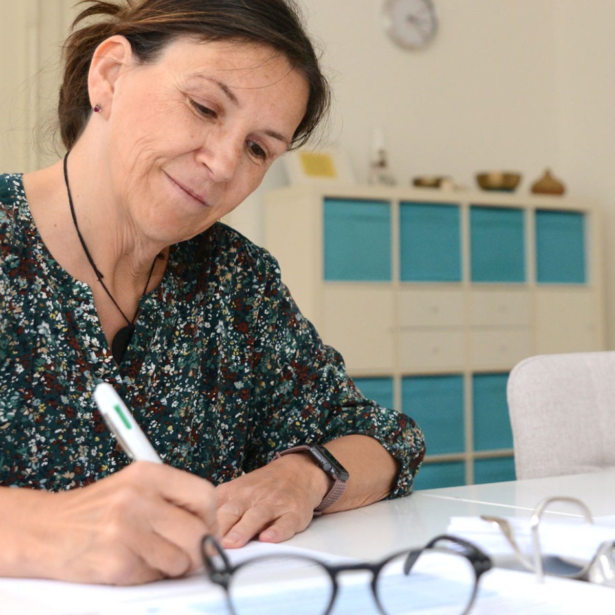 Teilnehmerin schreibt am Tisch Notizen, vor ihr ein Ordner und eine Brille